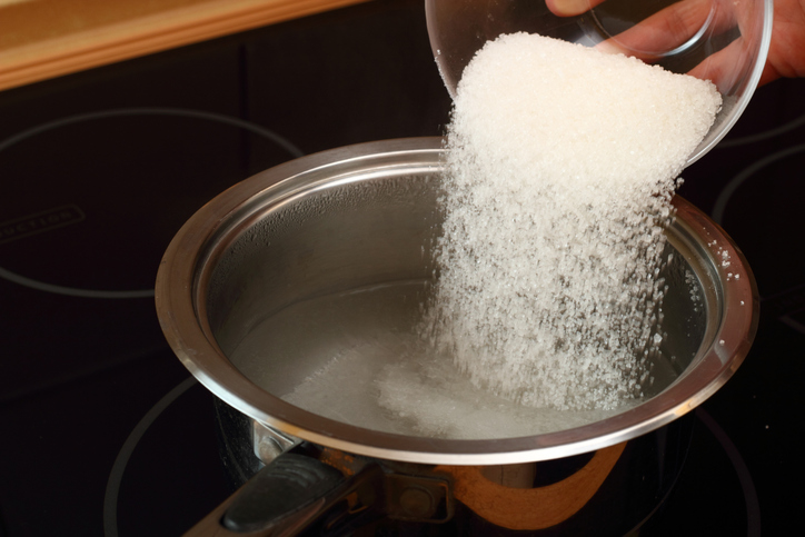 Sugar being poured into water boiling on the stove to make buttermilk icing.