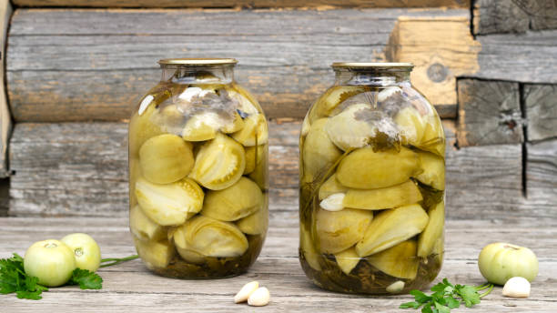 homemade pickled green tomatoes for winter in a glass jars with garlic and parsley. - pickled green tomatoes stock pictures, royalty-free photos & images