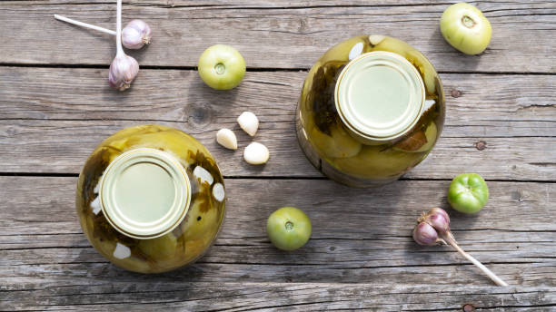 homemade pickled green tomatoes for winter in a glass jars with garlic and parsley. home conservation. top view. - pickled green tomatoes stock pictures, royalty-free photos & images