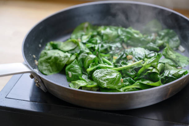 fried spinach leaves in a pan on the stove, healthy cooking concept - cooked spinach stock pictures, royalty-free photos & images