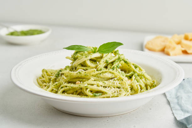 traditional italian pesto pasta spaghetti with pine nuts, garlic, basil, parmesan cheese. light gray table. homemade italian cuisine. vegetarian green pasta. - pesto stock pictures, royalty-free photos & images