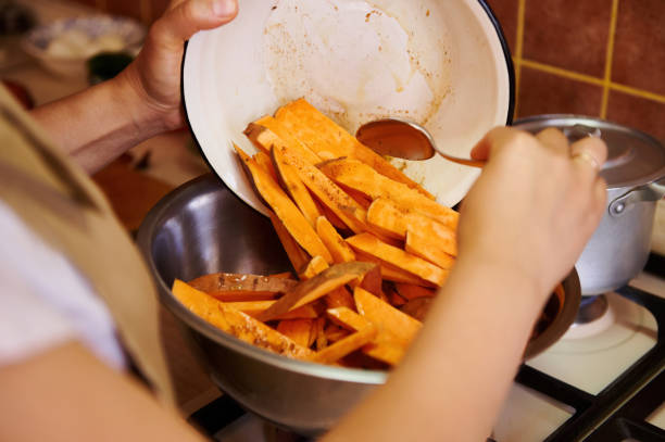 focus on slices of wholesome organic batata in a bowl, in the hands of a chef cooking healthy vegan meal at home kitchen - cutting sweet potato stock pictures, royalty-free photos & images