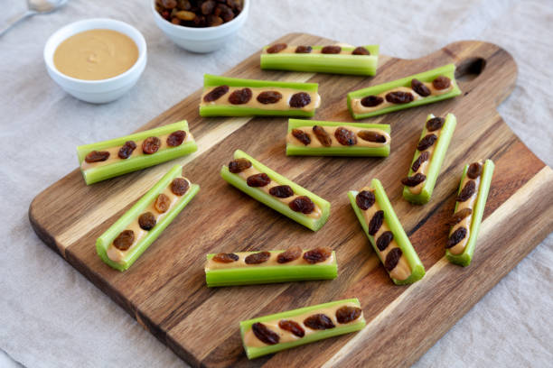 homemade ants on a log with celery, peanut butter and raisins on a wooden board, side view. - ants on a log snack stock pictures, royalty-free photos & images