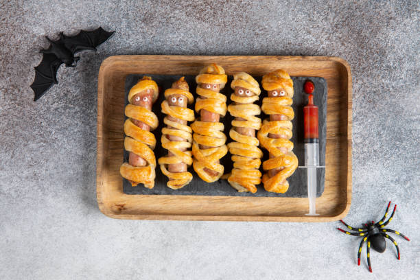 halloween mummy hot dogs. sausages with eyes wrapped in dough in wooden tray on concrete background. crazy funny halloween food. - mummy hot dog stock pictures, royalty-free photos & images