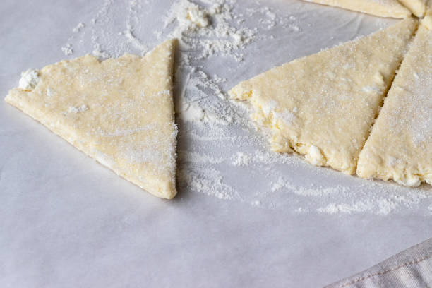 rolled raw curd dough cut into eight triangles sprinkled with sugar and one triangle of dough lies separately on baking paper on a linen tablecloth. the process of making curd bagels or croissants - crescent roll dough triangles stock pictures, royalty-free photos & images