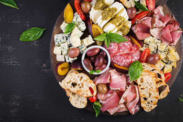 antipasto platter with ham, prosciutto, salami, blue cheese, mozzarella with pesto and olives on a wooden background. top view, overhead - antipasto platter stock pictures, royalty-free photos & images