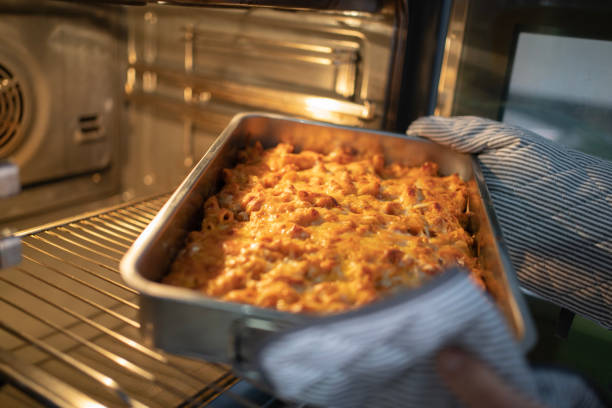 woman hands taking baked homemade macaroni with cheese with a crispy top out of the oven - mac and cheese oven stock pictures, royalty-free photos & images