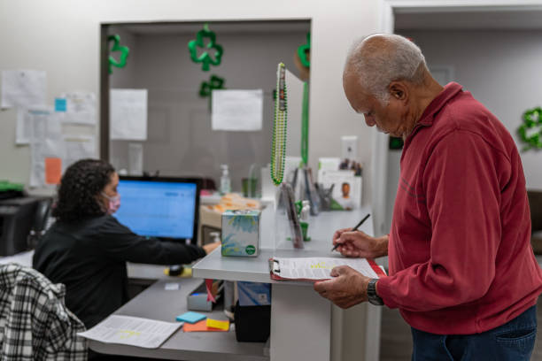 senior man completing paperwork at medical appointment - medicaid stock pictures, royalty-free photos & images