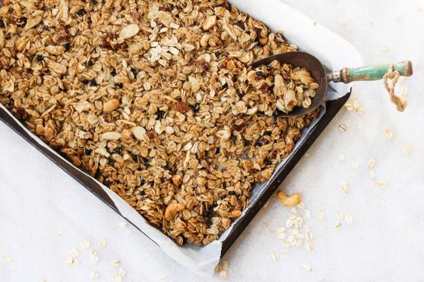 homemade granola in a parchment lined baking sheet, selective focus - granola homemade stock pictures, royalty-free photos & images