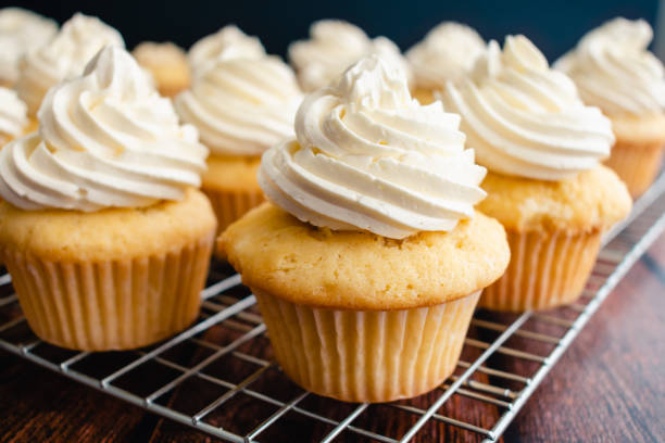 homemade vanilla cupcakes on wire cooking racks - vanilla cupcakes being iced stock pictures, royalty-free photos & images