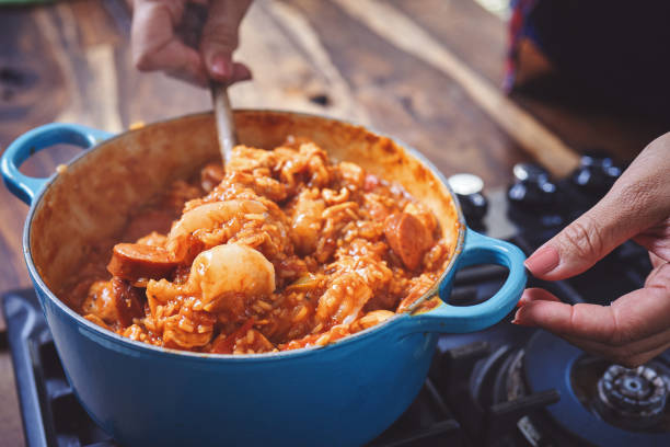 preparing cajun style chicken, shrimp and sausage jambalaya in a cast iron pot - seafood gumbo stock pictures, royalty-free photos & images